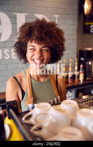 Smiling Female Owner Or Staff Serving Behind Counter In Coffee Shop Stock Photo