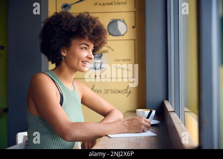 Female Customer In Coffee Shop Window Working Writing In Notebook Stock Photo