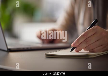 Close Up Of Man At Desk With Laptop Making Notes In Notebook Stock Photo
