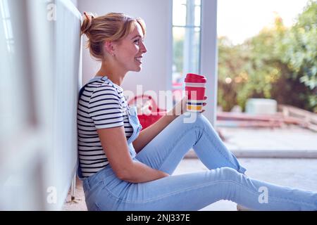 Woman Decorating Room At Home Sitting On Floor Taking A Break With Hot Drink In Reusable Cup Stock Photo