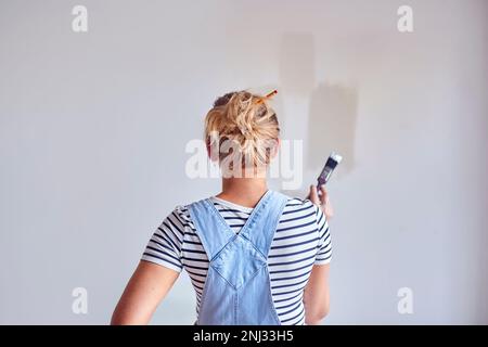 Rear View Of Woman Decorating Room In House Painting Tester Paint Colour Strips On Wall Stock Photo