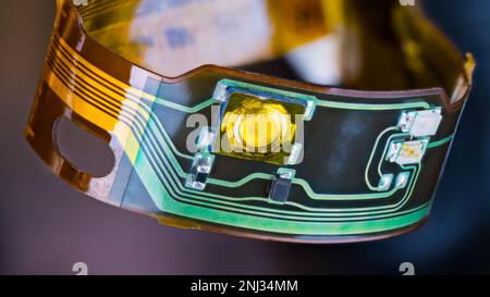 Flex printed circuit and small electronic components in plastic strip curled into circle on dark background. Closeup of flexible PCB from headphones. Stock Photo