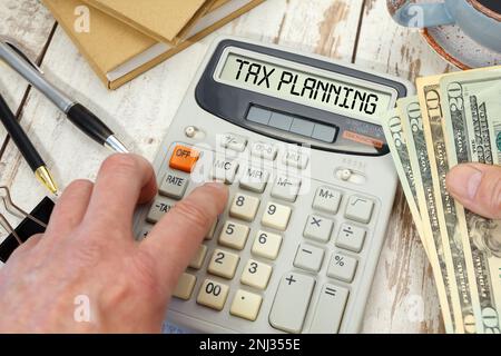Money in hand next to a calculator and office supplies. TAX PLANNING words on calculator. Stock Photo
