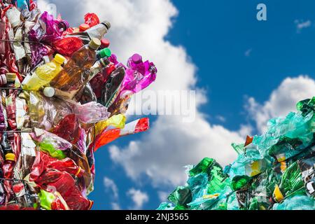 Plastic waste from used crumpled PET bottles in colored bales on a blue sky background with white clouds. Closeup of empty crushed beverage packagings. Stock Photo