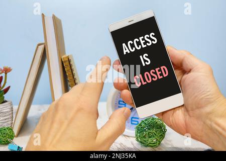 Smartphone in hand with the inscription ACCESS IS CLOSED next to office supplies Stock Photo