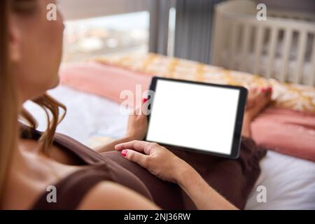 Pregnant Woman Relaxing On Bed At Home Watching Green Screen Digital Tablet Holding Stomach Stock Photo