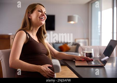 Pregnant Woman Working From Home On Laptop Sitting At Table Stock Photo