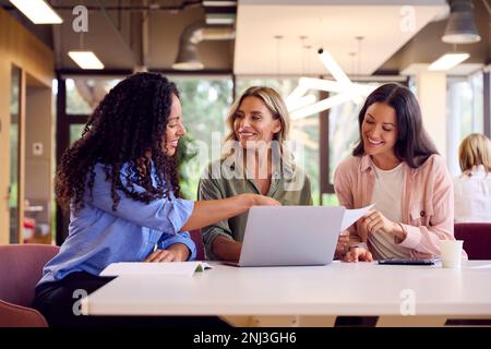 Multi-Cultural Female Business Team Sitting At Desk In Open Plan Office Collaborating On Project Stock Photo