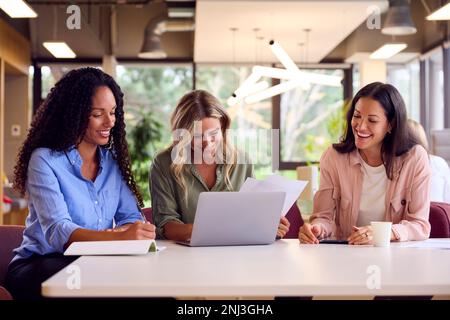 Multi-Cultural Female Business Team Sitting At Desk In Open Plan Office Collaborating On Project Stock Photo