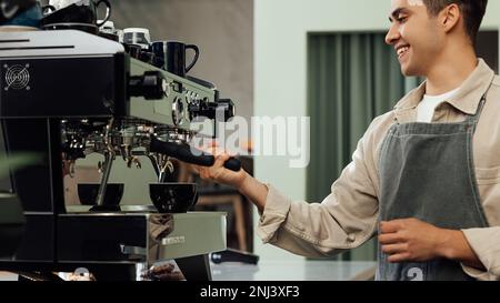Cropped shot of a young barista using a coffee machine. Smiling male barista adjusting coffee machine. Stock Photo