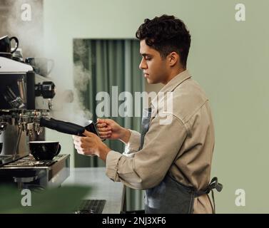 Side view of a male barista in an apron using a coffee machine. Barista using preparing cappuccino. Stock Photo