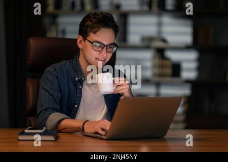 Overworked young man drinking coffee while working late at night Stock Photo