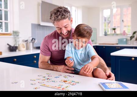 Mature Father At Home In Kitchen With Son Doing Jigsaw Puzzle Together Stock Photo