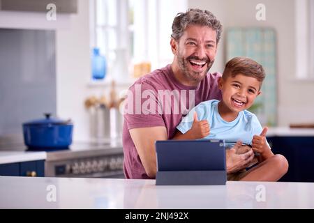 Mature Father At Home In Kitchen With Son Making Video Call On Digital Tablet Stock Photo