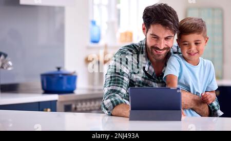 Father At Home In Kitchen With Son Using Digital Tablet Together Stock Photo