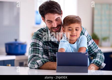 Father At Home In Kitchen With Son Using Digital Tablet Together Stock Photo