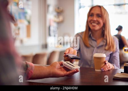 Female Customer Making Contactless Payment In Coffee Shop Using Mobile Phone Stock Photo