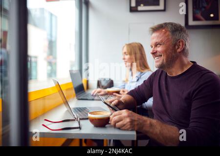 Customers In Coffee Shop Window Working On Laptops Using Mobile Phones Stock Photo