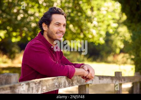 Smiling Casually Dressed Mature Man Leaning On Fence On Walk In Countryside Stock Photo
