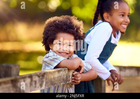 Portrait Of Two Smiling Children Leaning On Fence On Walk In Countryside Stock Photo