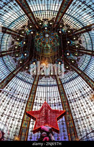 The dome of the building in Galeries Lafayette, the Parisian department store.  In the frame is the star on top of the Christmas tree. Stock Photo