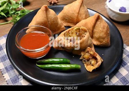 Picture of samosa or singara, a crispy and spicy triangle shape snack with a savoury filling of mashed potato, peas, and spices served in a black plat Stock Photo