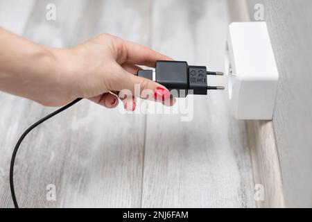 a man plugs a power supply into an outlet in a room. woman puts the device on charge. man plugging a plug into a socket Stock Photo
