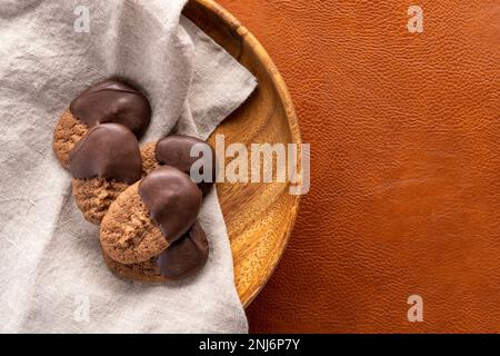 chocolate spritz cookies dipped in chocolate sitting on a wooden plate with a linen napkin on a tan leather background Stock Photo