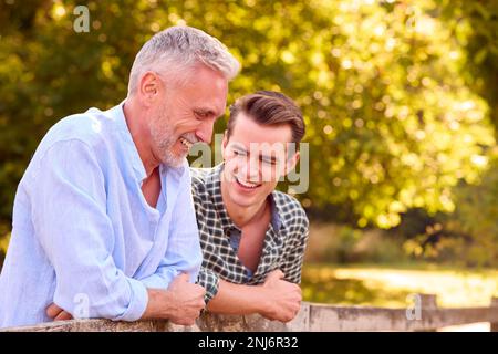 Mature Father With Adult Son Leaning On Fence Walking In Countryside Stock Photo