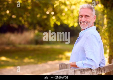Casually Dressed Mature Man Leaning On Fence On Walk In Countryside Stock Photo