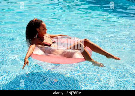Woman On Summer Holiday Floating On Inflatable In Swimming Pool Stock Photo