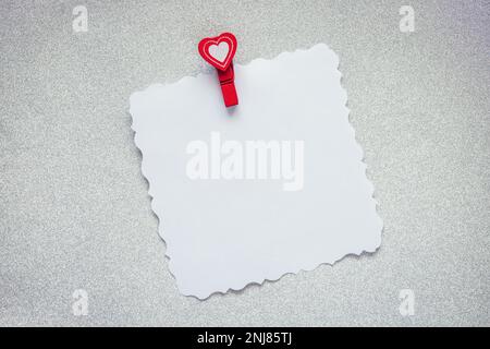 Note and heart shaped paper clip on gray silver background. Love message mock up, blank holiday greeting card. Stock Photo