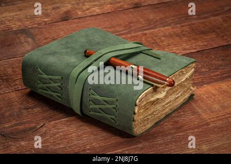 retro leather-bound journal with decked edge handmade paper pages with a stylish pen on a rustic barn wood table, journaling concept Stock Photo