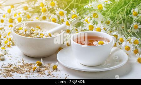 Rural still-life - cup of brewed chamomile tea on the background of a bouquet of daisies, closeup Stock Photo