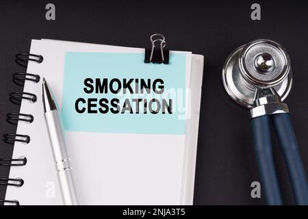 Medical concept. On a black surface, a stethoscope, a notebook, a pen and a blue sticker with the inscription - Smoking Cessation Stock Photo