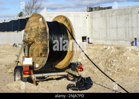 A trailer with a large spool of wooden black high voltage power cable at the construction site of a new large industrial facility Stock Photo