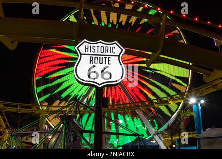 A picture of the Route 66 sign at night, with the Pacific Wheel in the back. Stock Photo