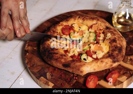 Person delicately slicing pizza on cutting board with sharp knife Stock Photo
