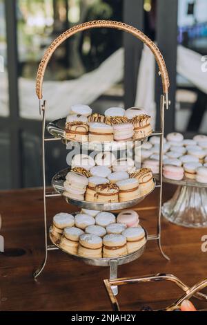 A three-tiered display stand filled with freshly-baked donuts and macarons positioned next to a decorative glass vase Stock Photo