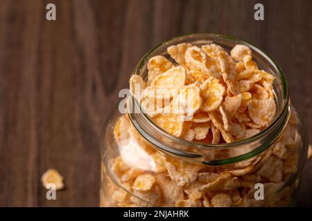 A glass jar filled with cereal flakes on a wooden surface Stock Photo