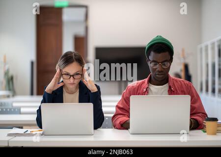 Concentrated serious students learning sitting in desktop in college lecture classroom with laptops. Stock Photo