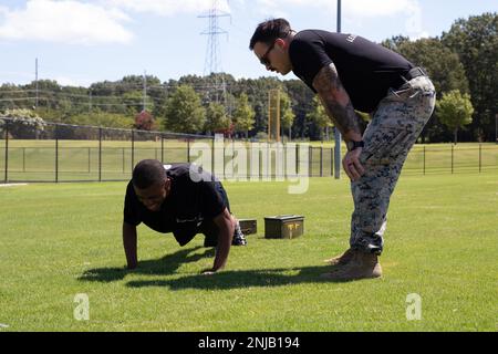 U.S. Marine Sgt. Danek Wisniewski, a recruiter with Marine Corps Recruiting Sub Station Tupelo, instructs a future Marine as he conducts push ups during a combat fitness workout in Tupelo, Mississippi, Aug. 6, 2022. The purpose of this workout was to introduce poolees in the Delayed Entry Program to the combat fitness test, which is an assessment that goes over the basic maneuvers and lifesaving carries that Marines use. Stock Photo