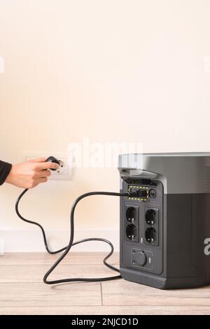 Woman inserting plug of portable solar station into socket at home Stock Photo
