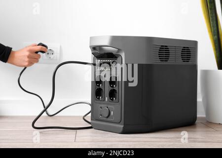 Woman inserting plug of portable solar station into socket at home Stock Photo