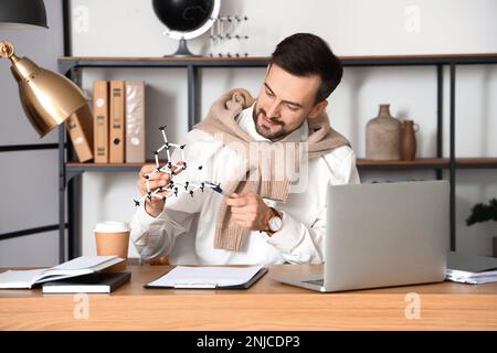 Male tutor with molecular model giving online Physics lesson at home Stock Photo