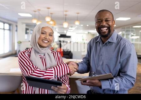 Happy diverse female and male business people shaking hands and looking at camera in office Stock Photo