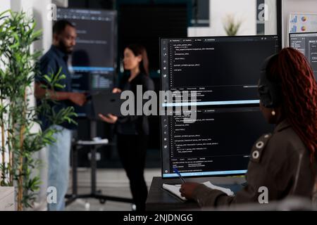 Multi ethnic team of software developers analyzing code on wall screen tv, using digital device and working with artficial intelligence. Programmers parsing cloud computing project with big data. Stock Photo