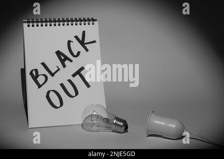 Notebook with the inscription 'Blackout' and an electric light bulb with a holder, illuminated by a flashlight. Monochrome picture Stock Photo