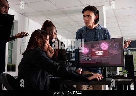 Diverse group of software developers having hacked server and security breach alert on computer display trying to solve hacking problem. Encountering critical error message flashing on screen. Stock Photo