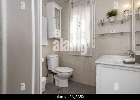 Bathroom with shower with sliding door screen, cream-colored tiles on walls and floors and bathroom cabinet with white porcelain sink with mirror Stock Photo